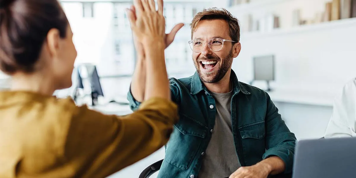 Zwei Kollegen geben sich im Sitzen ein High-Five am Büroarbeitsplatz.